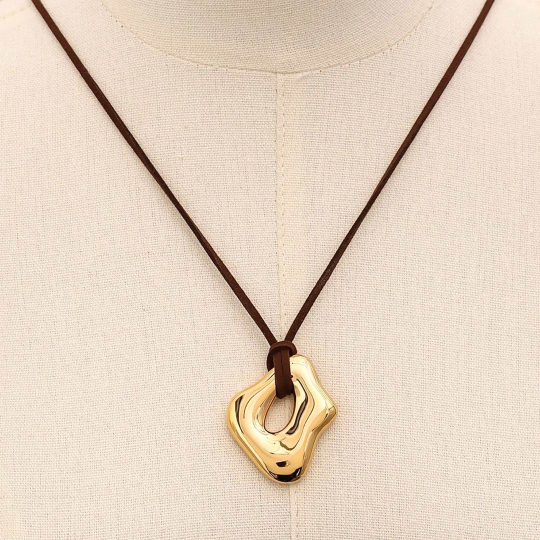 Primo piano del pendente scultoreo lucido con finitura in oro 18K e foro centrale.