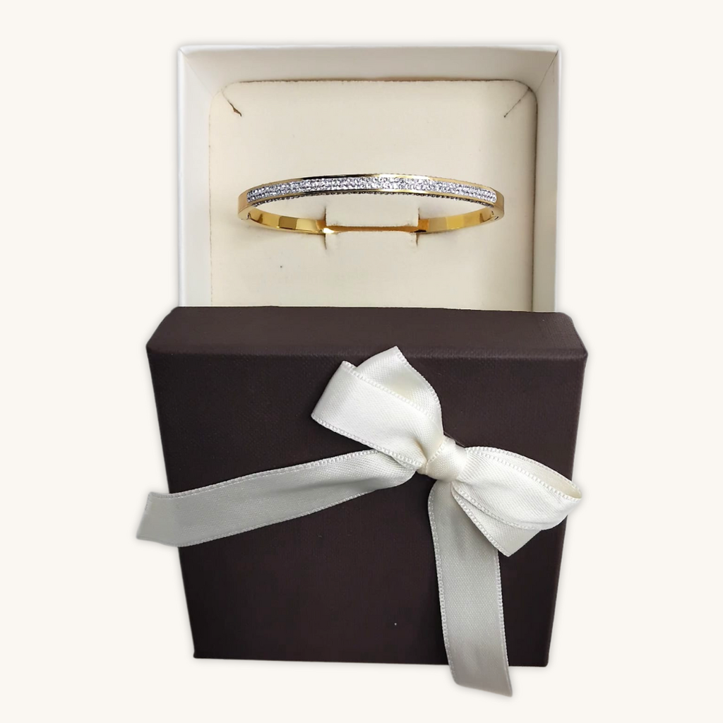 Bracciale rigido in oro con zirconi, nella confezione con fiocco bianco.