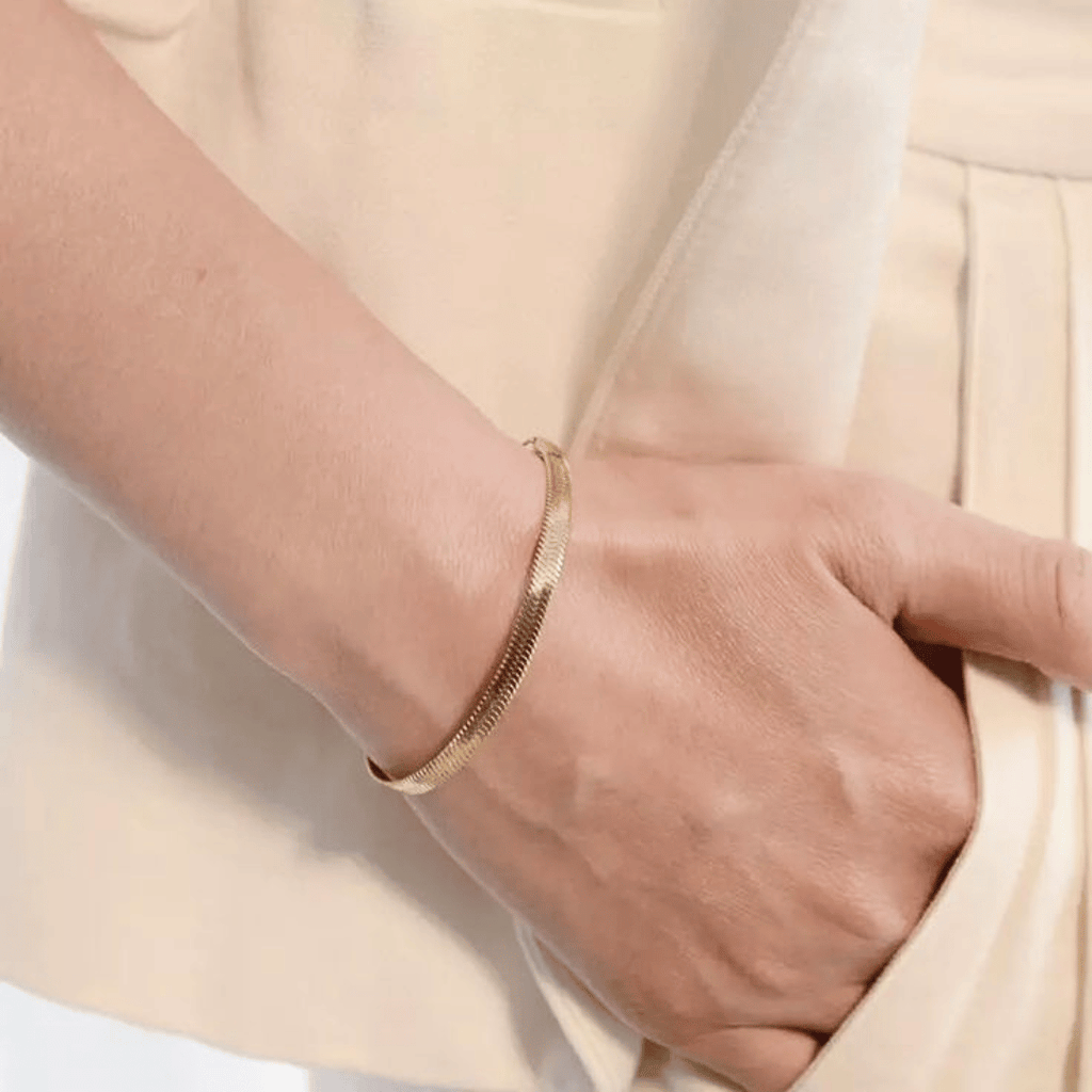 Bracciale dorato a maglia serpente indossato al polso, con chiusura visibile