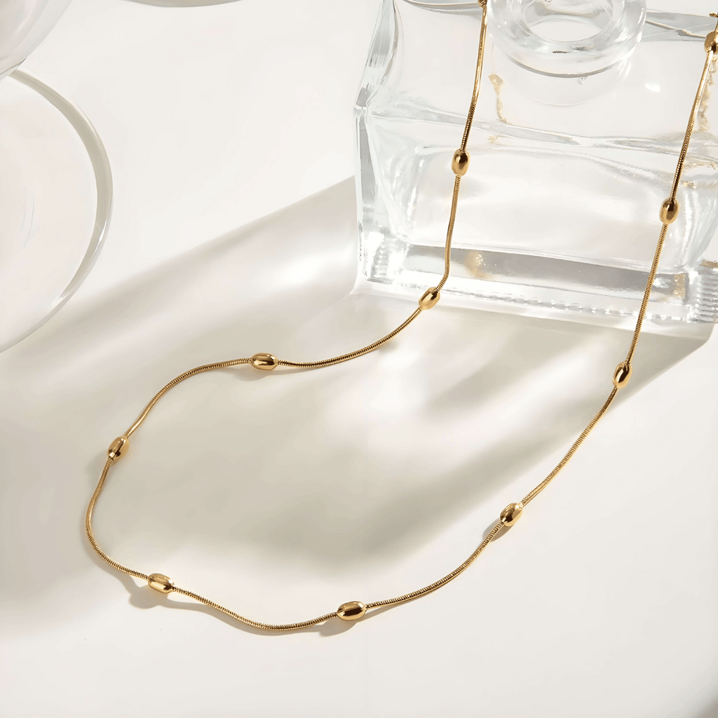 Collana oro 18K waterproof con maglie fluide ovali, stesa su superficie chiara