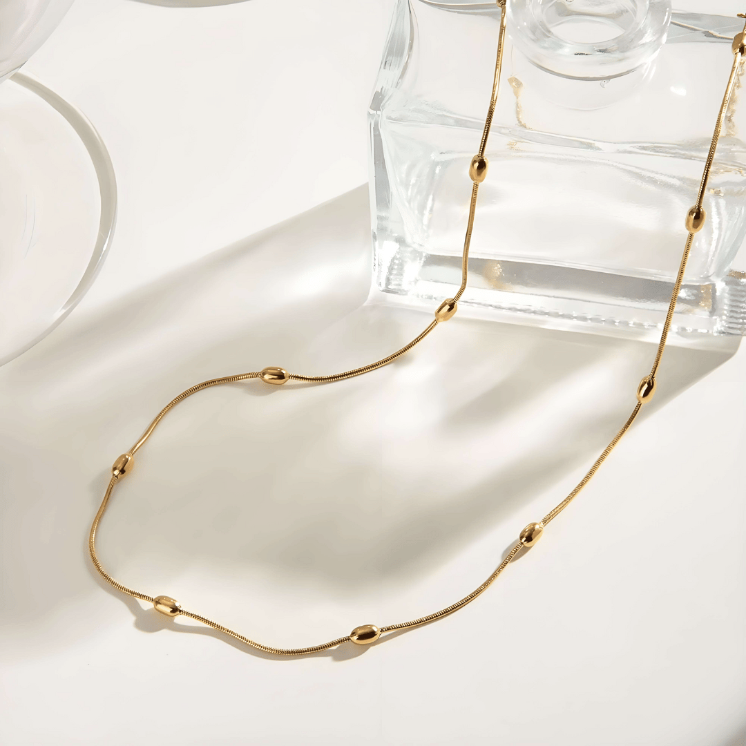 Collana oro 18K waterproof con maglie fluide ovali, stesa su superficie chiara
