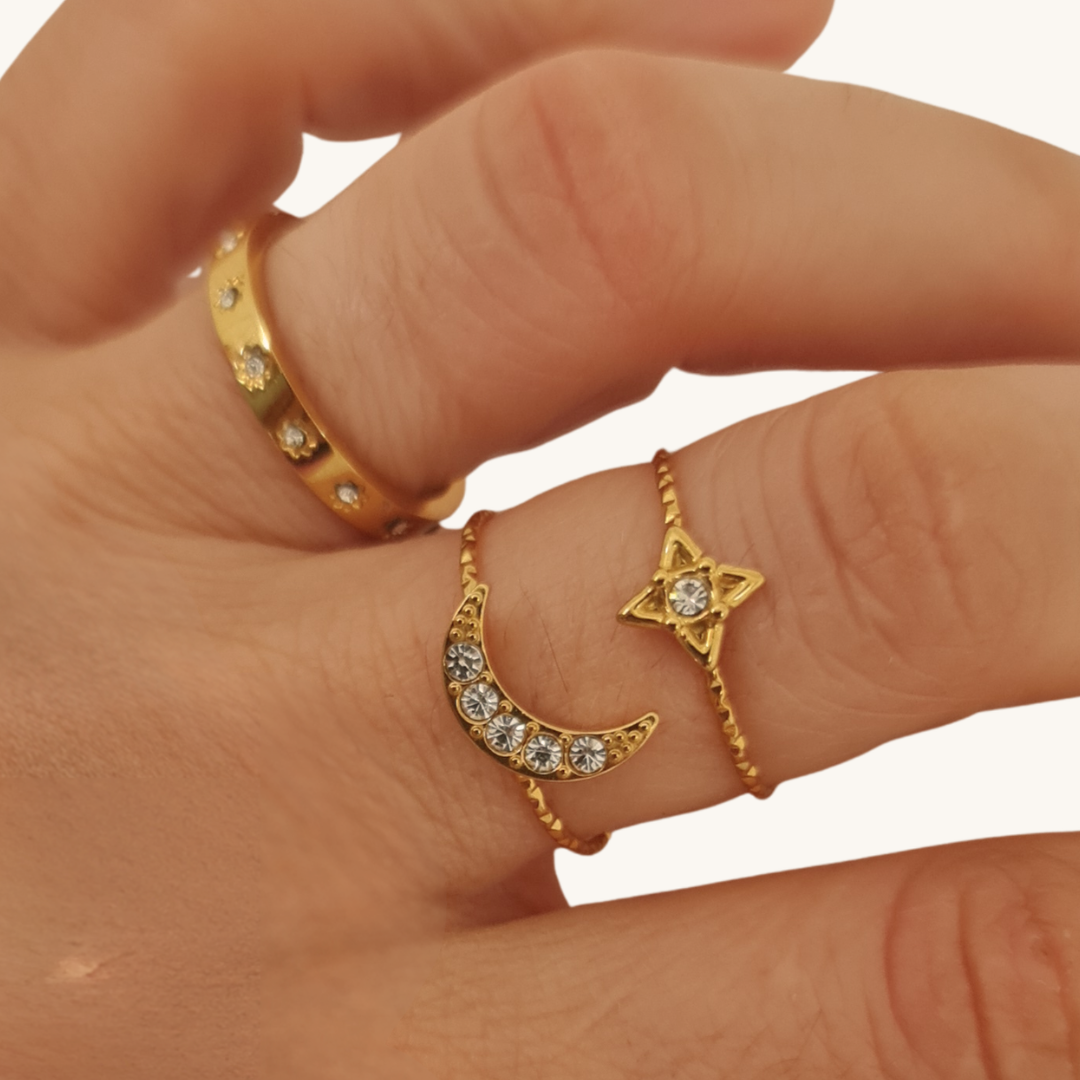 Set di anelli oro 18K con luna e stelle, indossati su dita con pietre chiare.