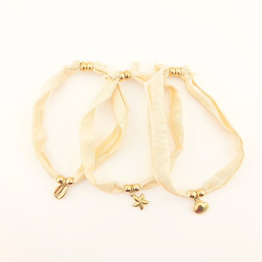 Tre bracciali in seta avorio con perle dorate e ciondoli a stella e conchiglie.