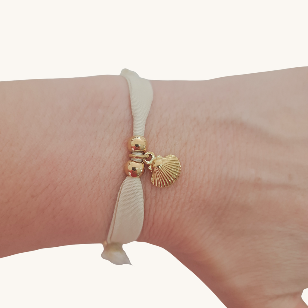 Bracciale in seta avorio con perle dorate e ciondolo a conchiglia sul polso.