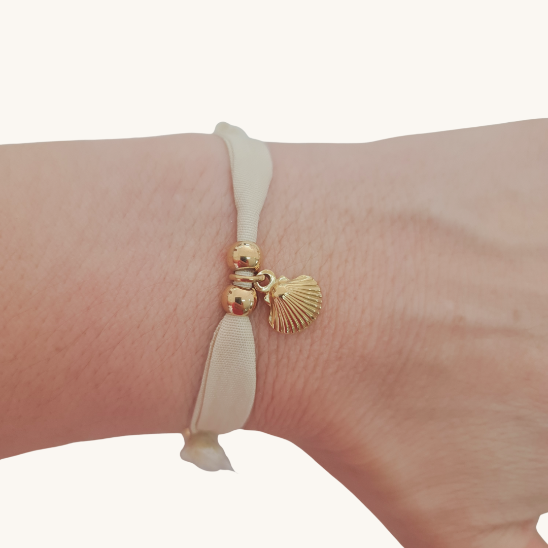 Bracciale in seta avorio con perle dorate e ciondolo a conchiglia sul polso.