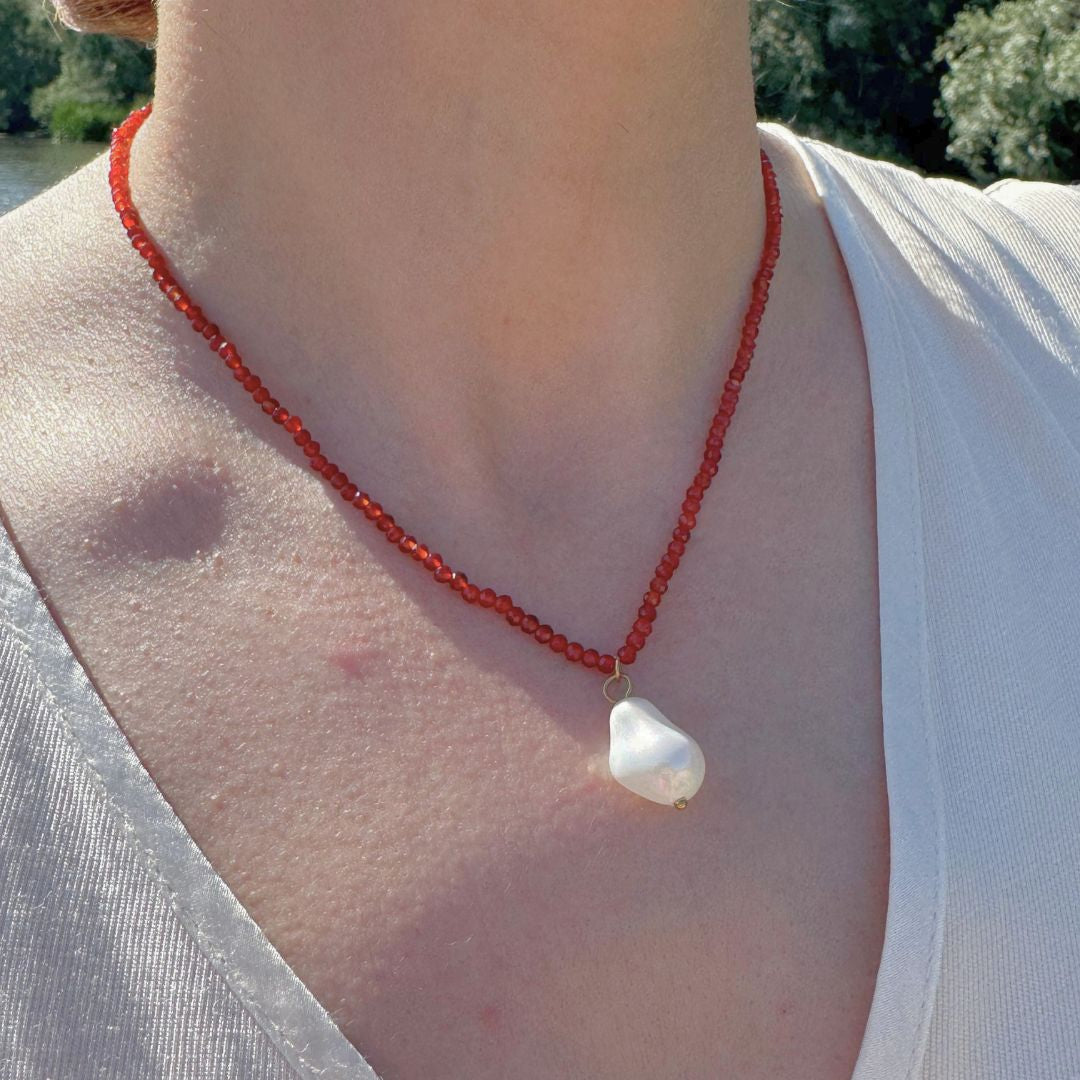 Collana di perline rosse con ciondolo perla bianca indossata al collo