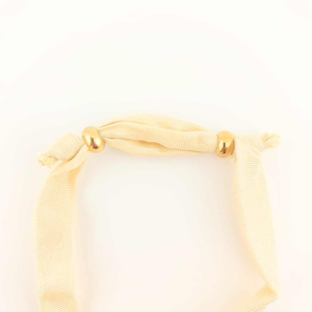 Bracciale in seta avorio con perle dorate e dettagli annodati.