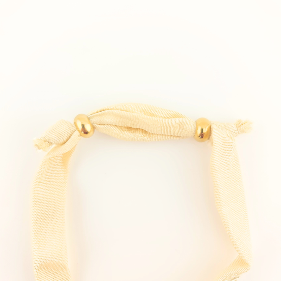 Bracciale in seta avorio con perle dorate e dettagli annodati.