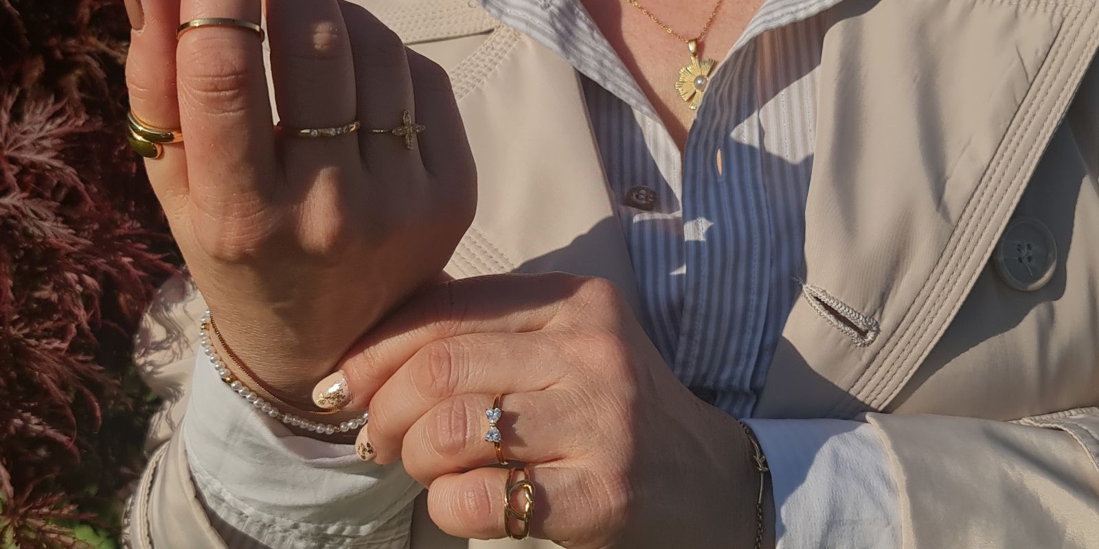 Dettaglio di mani femminili che mostrano una combinazione di anelli sottili in oro con zirconi e un bracciale di piccole perle bianche naturali.